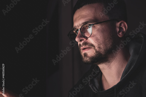 A man with glasses in the dark looks at the computer screen, copy space.