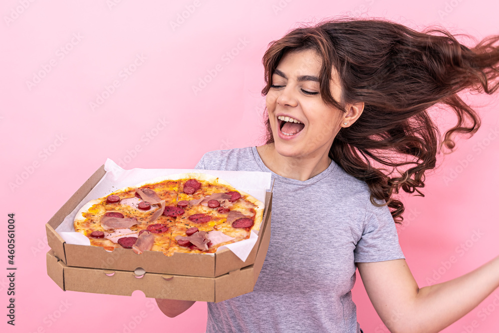 Beautiful girl holding pizza in a box for delivery on a pink background.