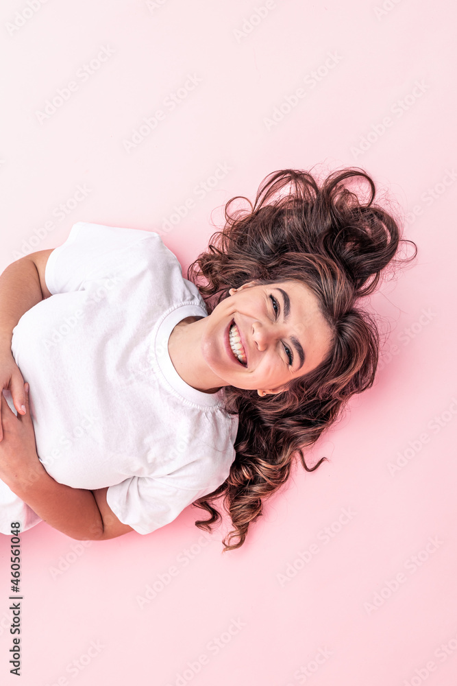 Cheerful brunette girl laughs lying on a pink background. Cheerful brunette girl laughs lying on a pink background.