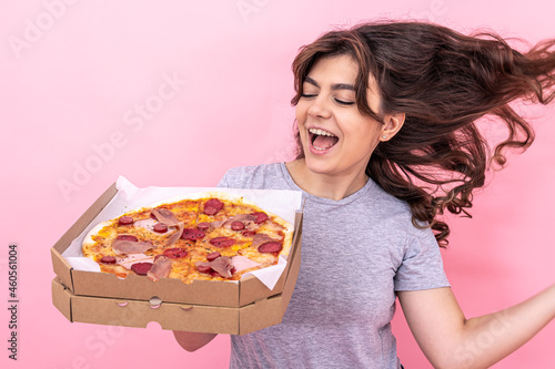 Beautiful girl holding pizza in a box for delivery on a pink background.