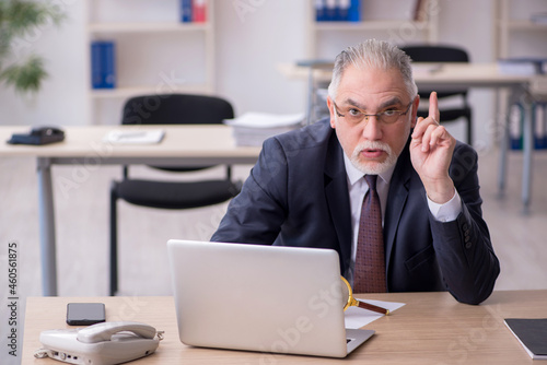 Old male employee sitting at workplace