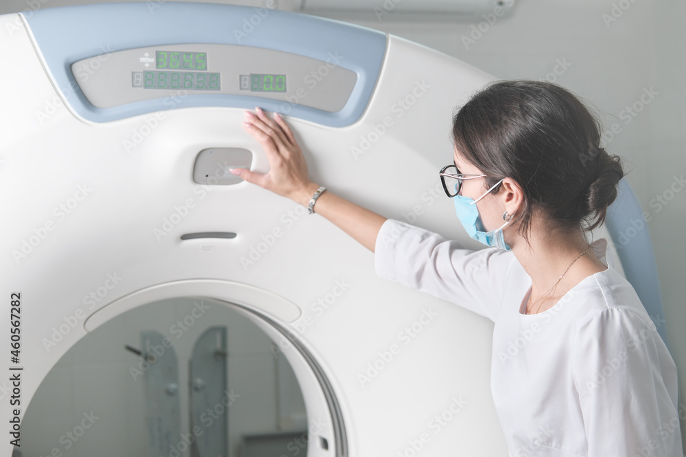 woman x-ray doctor adjusting computer tomography scanner machine to make CT test. female technician wearing face mask working in a hospital or clinic. woman x-ray doctor adjusting computer tomography scanner machine to make CT test. female technician wearing face mask working in a hospital or clinic.