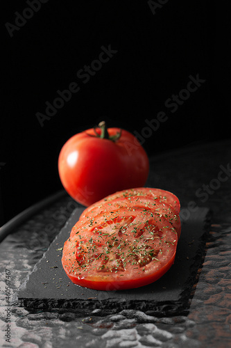 Sliced ​​and whole tomatoes with herbs. Black cutting board.
