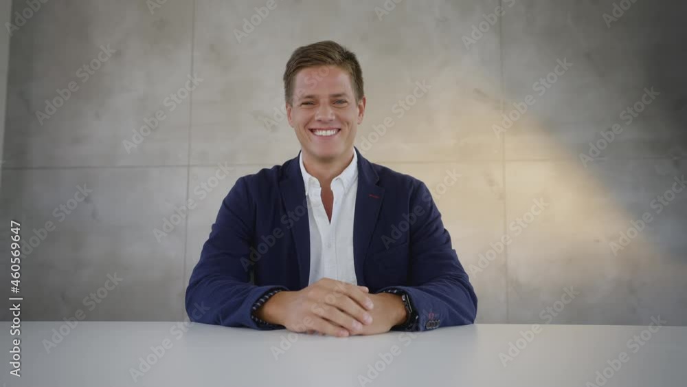 Smiling Caucasian man sitting in front of camera and having video call. Tilled background. Hands clasped on table. Smiling Caucasian man sitting in front of camera and having video call. Tilled background. Hands clasped on table.