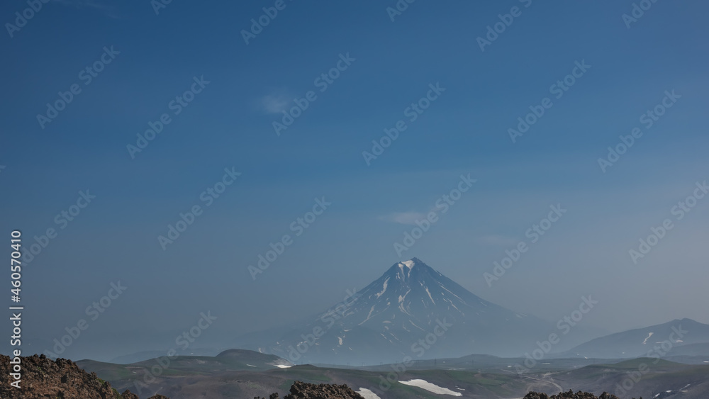 A beautiful conical volcano with snow-covered slopes against a blue sky with light clouds. Copy  space. Kamchatka. Stratovolcano Vilyuchinsky