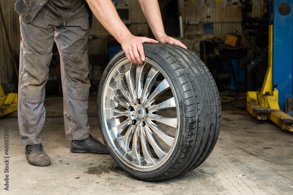 An auto mechanic holds a wheel of a car. Change of car tires according to the season