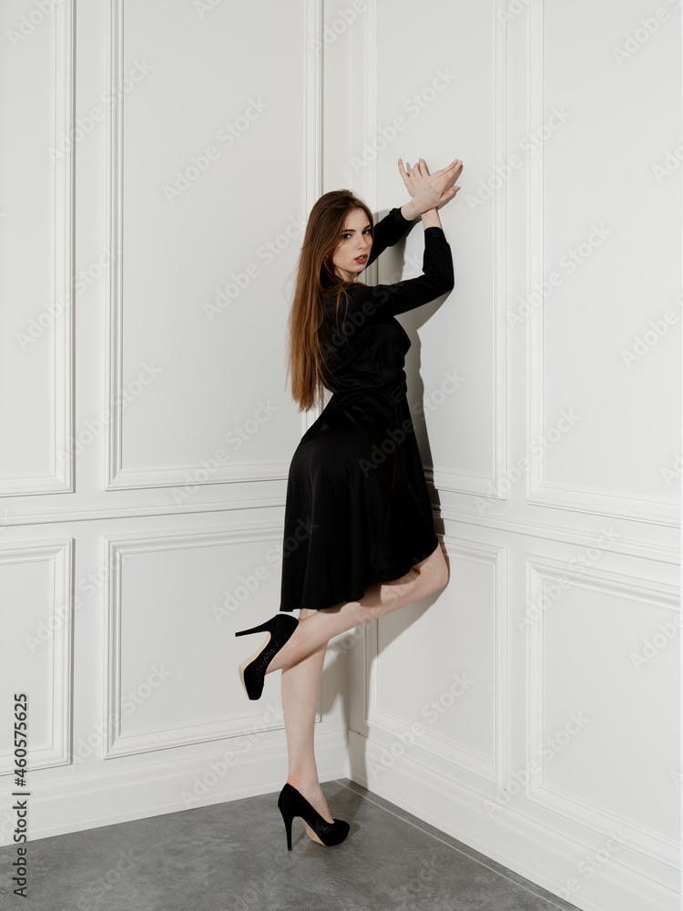 Fashion model stands in the corner of the room, leaning to the wall and lifting one leg Fashion model stands in the corner of the room, leaning to the wall and lifting one leg