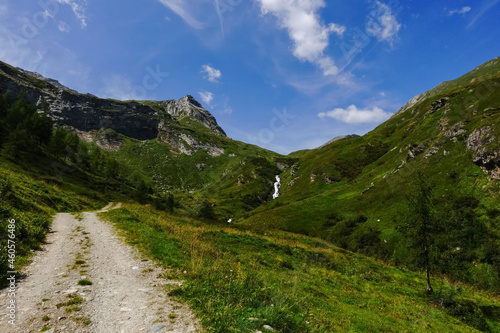 long dirt road through green mountains with a waterfall in the distance