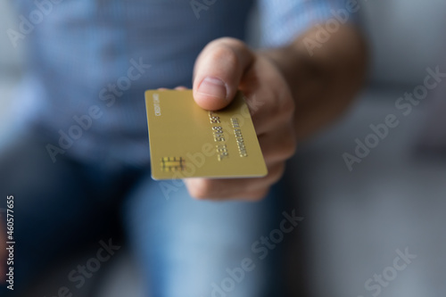 Crop close up young man holding showing gold credit card, giving at camera, customer paying for goods by debit card, shopping and purchasing, bank worker businessman offering service to client