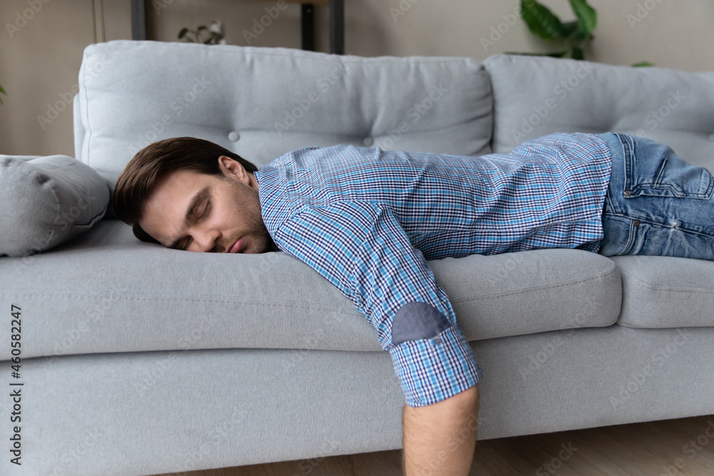 Exhausted man lying on comfortable couch at home, sleeping, taking day nap  or daydreaming, tired overworked young male fall asleep on sofa after  difficult working day, fatigue and tiredness concept Stock-Foto