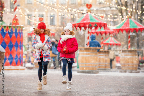 Children, red-haired sisters, walk along with shopping toys in their hands at a festively decorated Christmas market in the city.