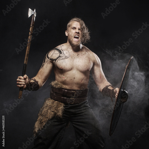 Viking warrior in full with ax aggressively attacks on dark background