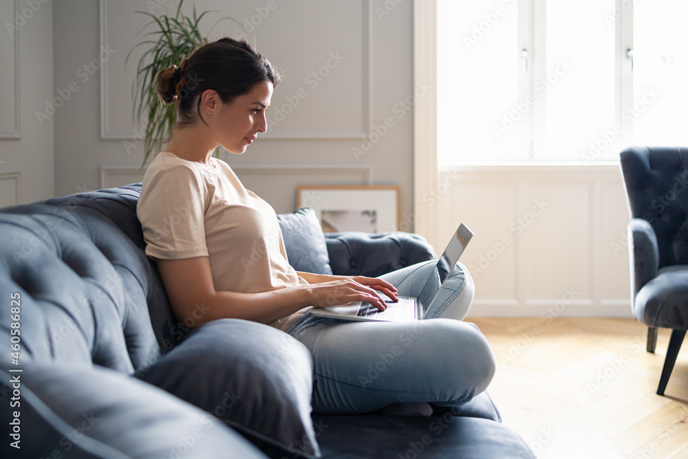Young woman surfing the Internet on laptop while relaxing on sofa at home.