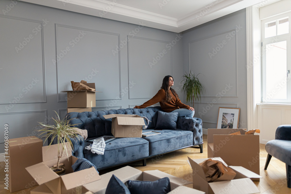 Fototapeta premium Smiling woman day dreaming in her new living room.