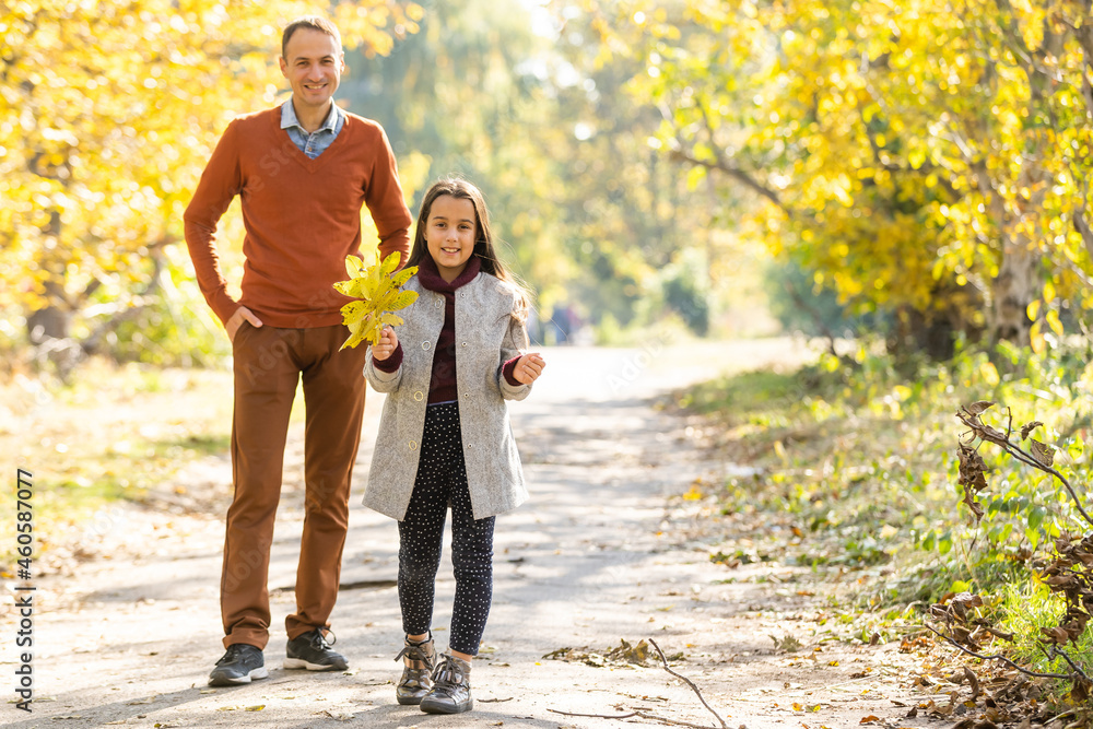 Obraz premium Adorable little girl with happy father walking in autumn park on a sunny day