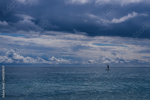 A man on a board with a paddle in the sea is surfing on vacation against a cloudy dark sky