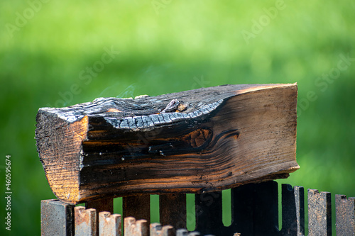 Smoking piece of wood on metal grill. Green lawn in Valakampiai Park, Vilnius, Lithuania. Public outdoor fireplace for grilling and picnic. Selective focus on the details, blurred background.