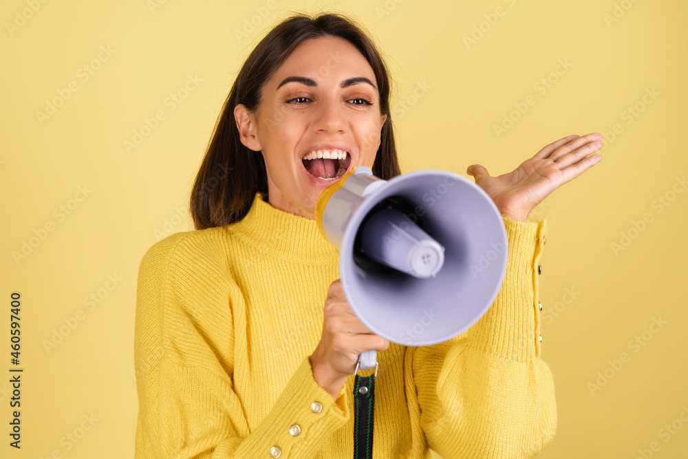 Young woman in yellow warm sweater with megaphone speaker screaming happy excited Young woman in yellow warm sweater with megaphone speaker screaming happy excited