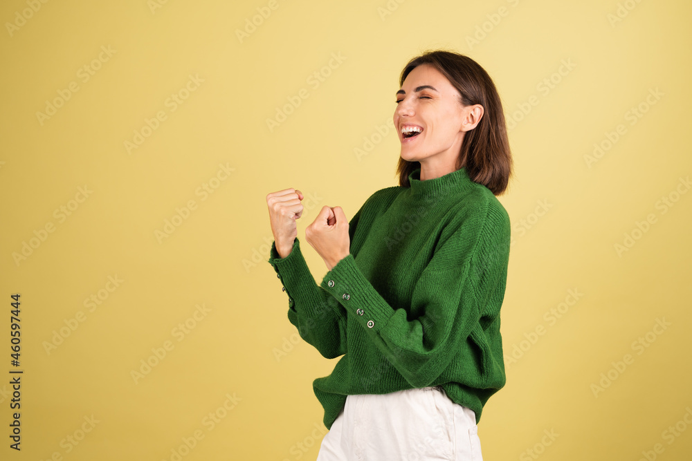 Young woman in green warm sweater happy excited shows winner gesture Young woman in green warm sweater happy excited shows winner gesture