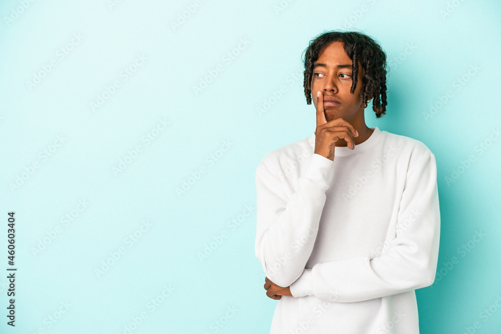 Young african american man isolated on blue background looking sideways with doubtful and skeptical expression.