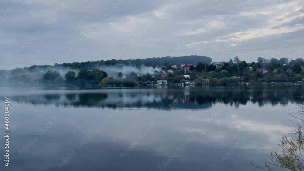 Evening view of the lake on which the sky is reflected, fishermen on boats catch fish. Smoke from burning grass spreads over the water Evening view of the lake on which the sky is reflected, fishermen on boats catch fish. Smoke from burning grass spreads over the water