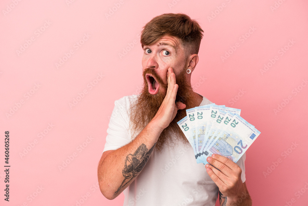 Young caucasian ginger man with long beard holding banknotes isolated on pink background is saying a secret hot braking news and looking aside Young caucasian ginger man with long beard holding banknotes isolated on pink background is saying a secret hot braking news and looking aside