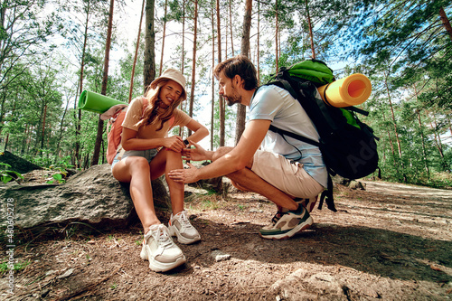 A pair of hikers with backpacks in the woods. The woman bruised her leg, felt pain and sat down on a stone. Camping, travel, hiking.