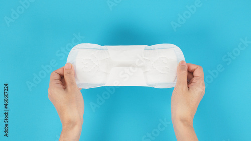 Hand is hold a sanitary napkin with wings top angle view on blue background.sanitary napkin for day use.