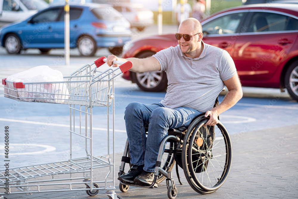 Person with a physical disability pushing cart in front of himself at supermarket parking Person with a physical disability pushing cart in front of himself at supermarket parking