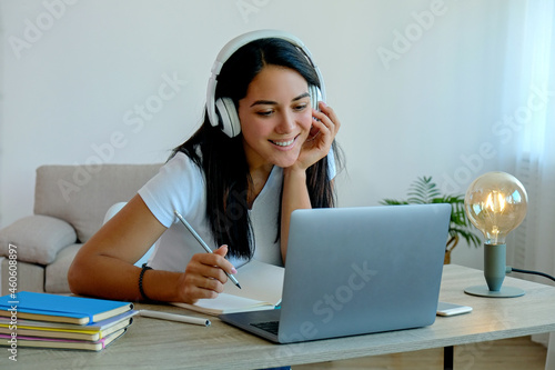 Online education concept. Young beautiful brunette woman watching an online lesson, writing in her notebook. Portrait of female student studying at home with laptop. Close up, copy space, background.