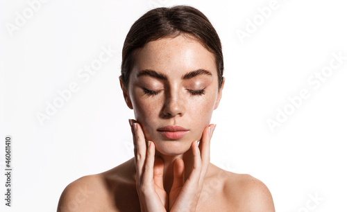 Skin care. Beauty face of young woman with closed eyes, gently touching soft, natural facial skin after shower, concept of cosmetology and skincare products, white background