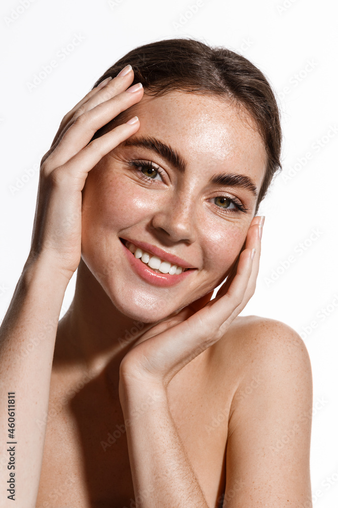 Vertical portrait of beautiful girl smiling at camera, touching natural face without makeup, healthy glowing facial skin and white teeth, standing over white background Vertical portrait of beautiful girl smiling at camera, touching natural face without makeup, healthy glowing facial skin and white teeth, standing over white background