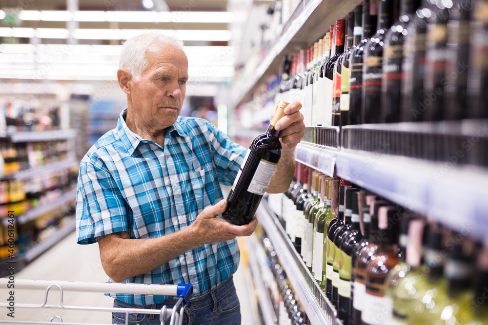 old age man examines bottle of vermouth in alcoholic section of supermarket