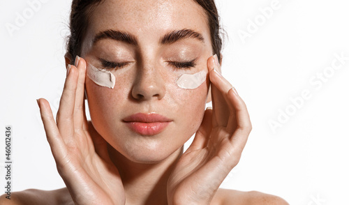 Close up beauty girl with freckles and thick eyebrows, applying moisturizing skincare cream, lotion or mask for skin lifting and anti-aging detoxifying effect, white background