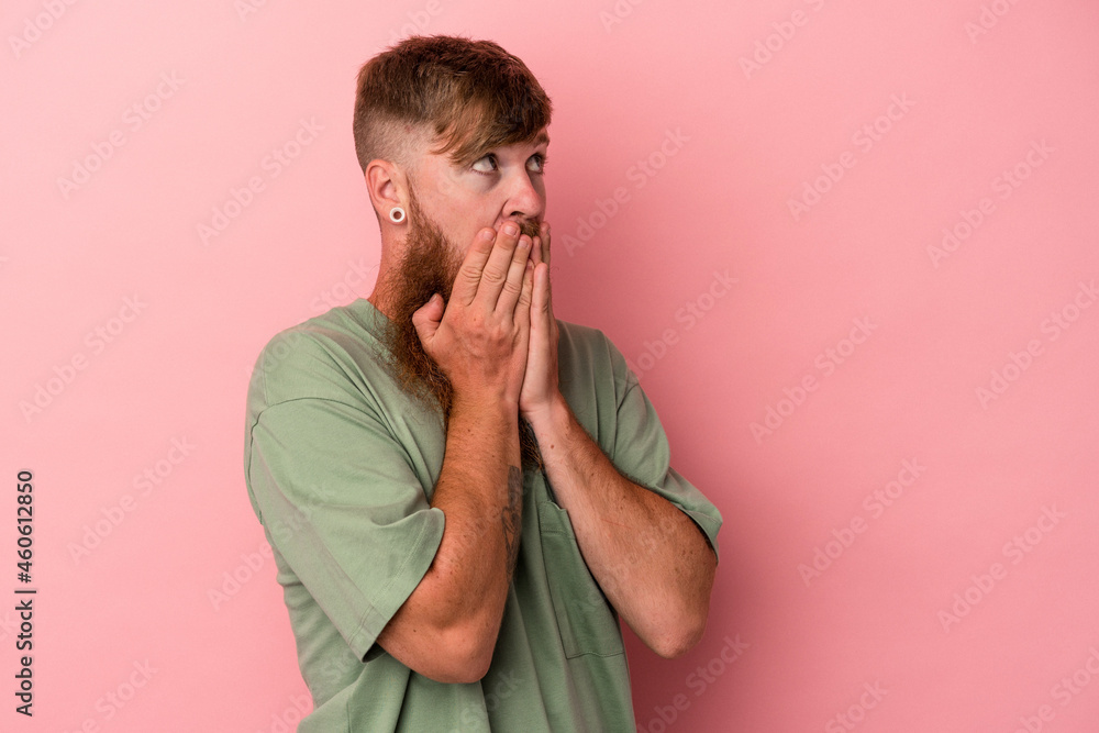 Young caucasian ginger man with long beard isolated on pink background thoughtful looking to a copy space covering mouth with hand. Young caucasian ginger man with long beard isolated on pink background thoughtful looking to a copy space covering mouth with hand.