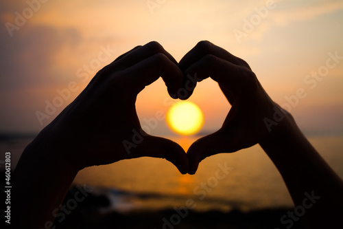 Sunset heart. Hand heart frame shape silhouette made against the sun and sky of a sunset on a deserted empty beach