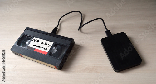 A video tape labeled as '20th century memories' plugged to a hard disk drive as a symbol of data transfer from analog to digital.