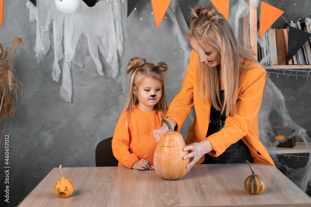 a woman and a girl in make a jack-o-lantern out of large pumpkins for the celebration of halloween. Cut with a knife, take out the pulp with seeds.
