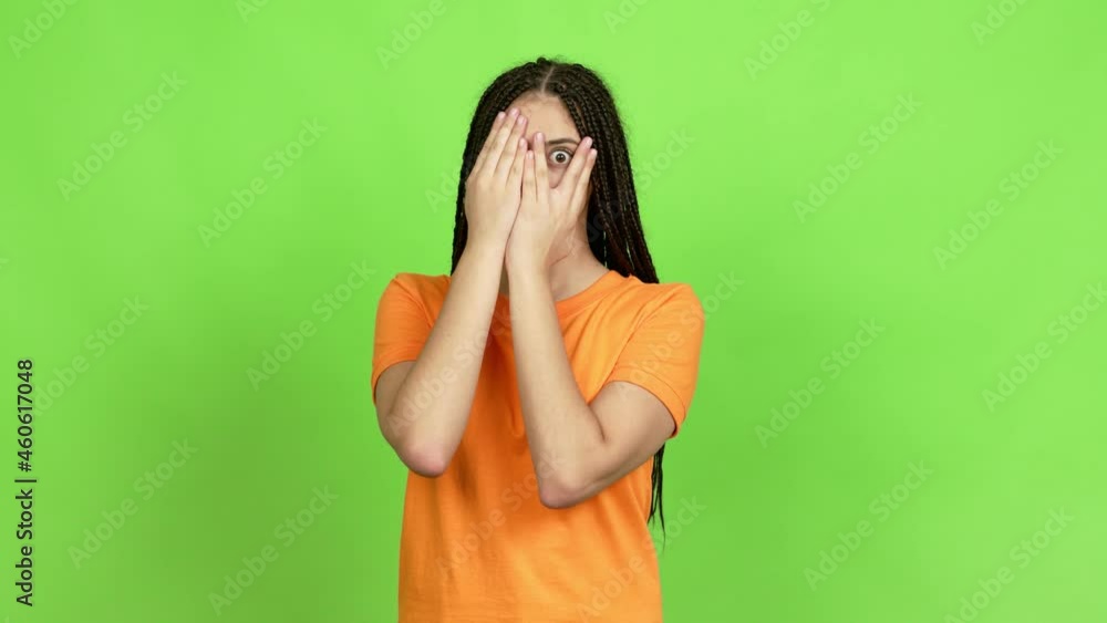 Teenager girl with braids covering eyes by hands and looking through the fingers over isolated background Teenager girl with braids covering eyes by hands and looking through the fingers over isolated background