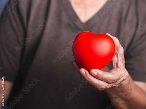 Fototapeta Naklejka Na Ścianę i Meble -  Hand of a senior woman holding a red heart shape. Close-up photo. Aged people and healthcare concept