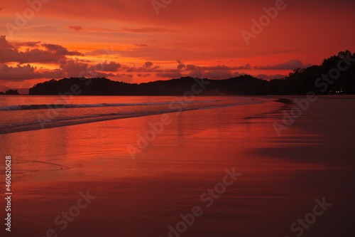 Roter Sonnenuntergang an langem Sandstrand mit flachen Wellen und Reflexionen Sillhouette