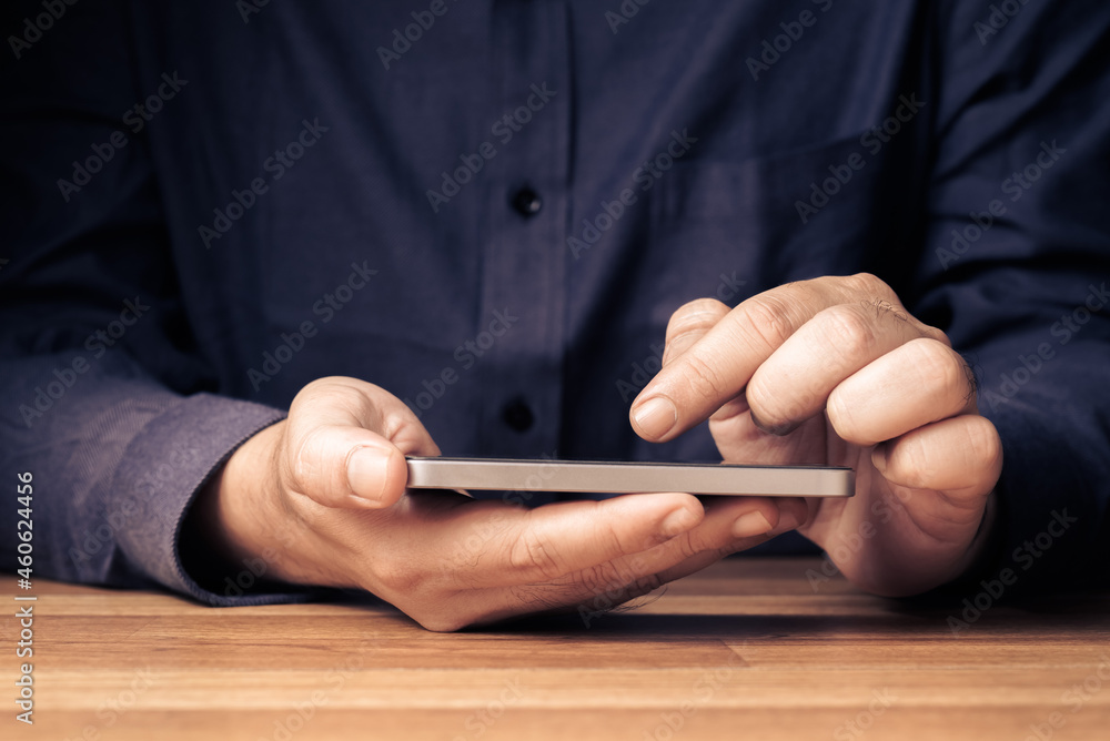 Closeup man going to touch the screen of mobile phone in his hand on the wood table Closeup man going to touch the screen of mobile phone in his hand on the wood table