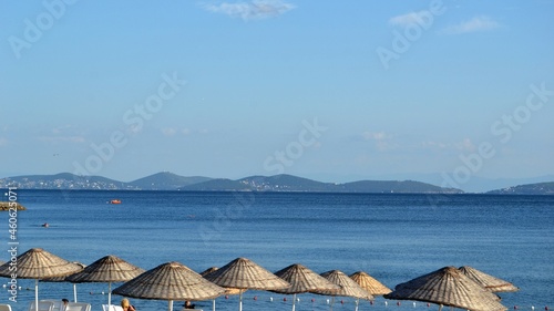 Beach straw umbrellas on coast of Marmara sea under blue sky with horizon in Istanbul during summer.