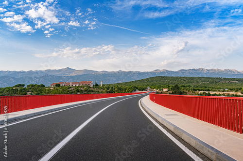 Red Maslenica Bridge, Croatia. Large red metal bridge crosses the Adriatic sea in Maslenica, Croatia and leads toward the majestic Velebit mountain range.