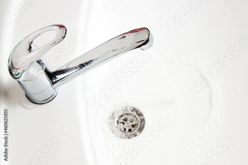 Water tap with flowing water into white sink