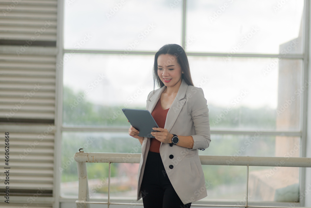 Portrait of an Asian businesswoman in a suit holding coffee and digital tablet in the office.