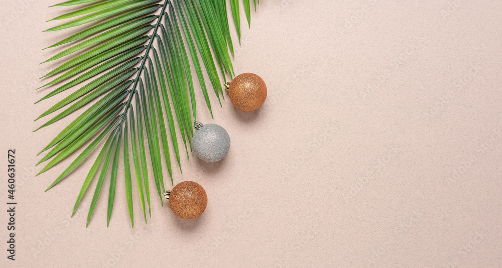 Artificial palm branch and Christmas balls on beige craft paper. Christmas composition. Top view, flat lay, wide composition