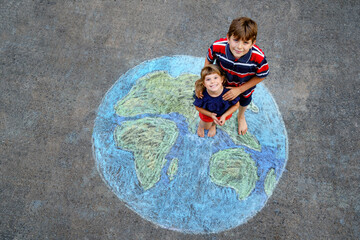 Little preschool girl and school kid boy with earth globe painting with colorful chalks on ground. Happy earth day concept. Creation of children for saving world, environment and ecology.