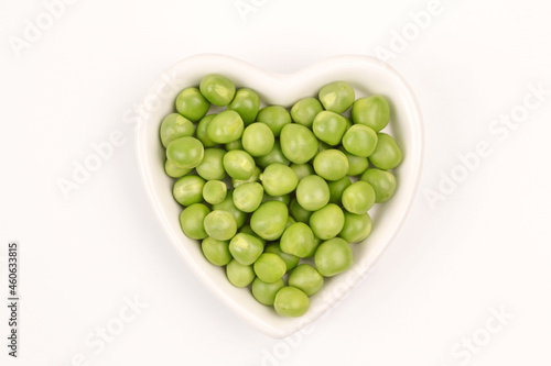 Green peas are lying in a white plate in the shape of a heart on a white background.Cultivation and care of agriculture, agronomy, breeding, vegetarianism, protein production, sports nutrition.