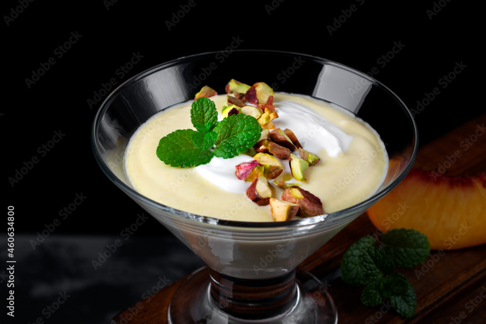 Mango dessert with yogurt topped with pistachio and mint in glass bowl against the black background. Exquisite dessert Mango dessert with yogurt topped with pistachio and mint in glass bowl against the black background. Exquisite dessert